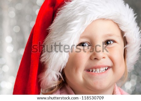 Happy baby girl in christmas hat, against sparkling silver background