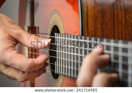 Man hands closeup playing red classical guitar, focus on right hand fingers with nails in a position.