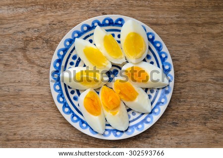 Two colors yolk, sliced hard boiled eggs in a blue decorated plate on wooden kitchen table. One egg yolk with yellow color, the other one orange.