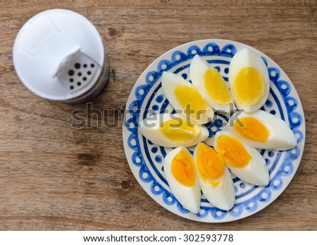 Two colors yolk, sliced hard boiled eggs in a blue decorated plate on wooden kitchen table. One egg yolk with yellow color, the other one orange. Salt shaker.