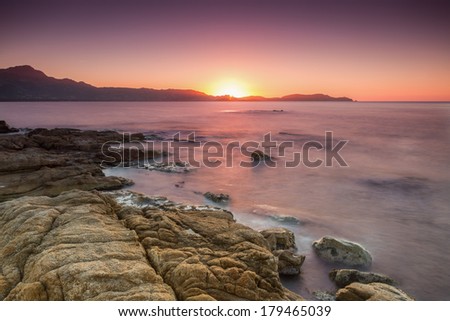 The sun setting over the town of Calvi in the Balagne region of Corsica with rocks and sea in the foreground