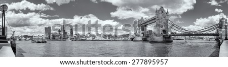 Black & white panorama of Tower Bridge, the Tower of London and the city with the river Thames in foreground with clear skies and fluffy clouds