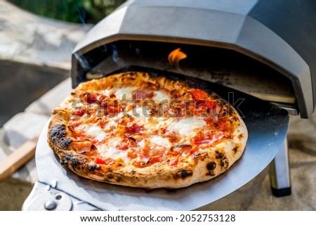 Making homemade pizza in portable high temperature gas  oven. Delicious pizza is baking in gas oven furnace for home made Neapolitan pizza. Special gas fueled pizza oven for picnic or party.