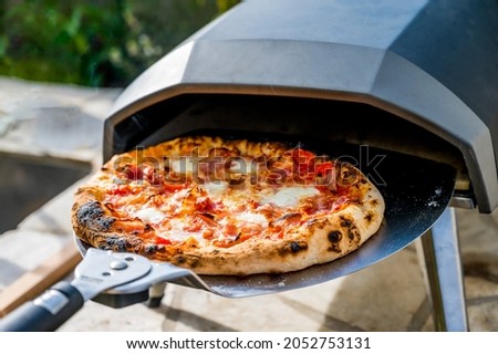 Making homemade pizza in portable high temperature gas  oven. Delicious pizza is baking in gas oven furnace for home made Neapolitan pizza. Special gas fueled pizza oven for picnic or party.