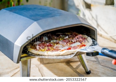 Making homemade pizza in portable high temperature gas oven. Delicious pizza is baking in gas oven furnace for home made Neapolitan pizza. Special gas fueled pizza oven for picnic or party.