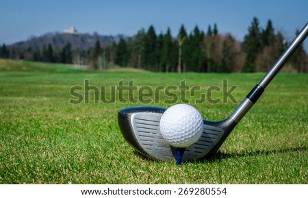 chipping a golf ball onto the green with driver golf club. Green grass with forrest and a castle in the background. Soft focus or shallow depth of field.