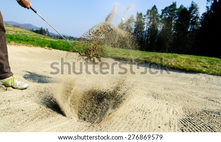 Golfer hitting out of a sand trap. The golf course is on the sand. Sand making splashes