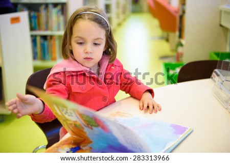Little girl is browsing a book in the library. A child is looking at the books in the library deciding which one to take home. Children creativity and imagination.