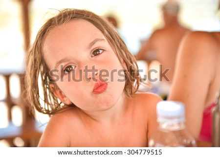 Little girl with wet hair is making a kiss gesture in a beach resort at sea after swimming in tropical sea. Vacation, lifestyle, happiness. No worries.