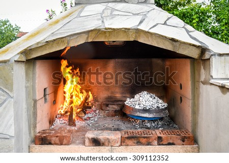 Cooking of traditional Balkan Greek Mediterranean Croatian meal Peka in metal pots called sac sach or sache or a metal lid. Fireplace with open fire and burning coals.