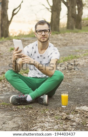 Young man drinking orange juice outdoor while looking at tablet
