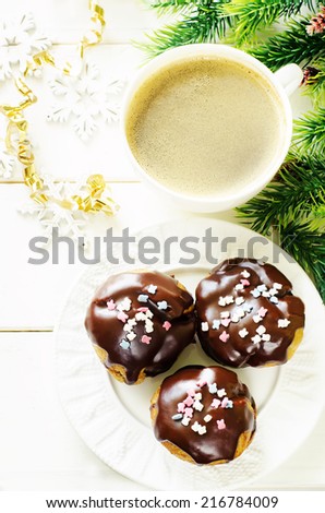 profiteroles with chocolate icing and colored powder and cup of coffee on a light wood background. tinting. selective focus on the middle of left profiterole