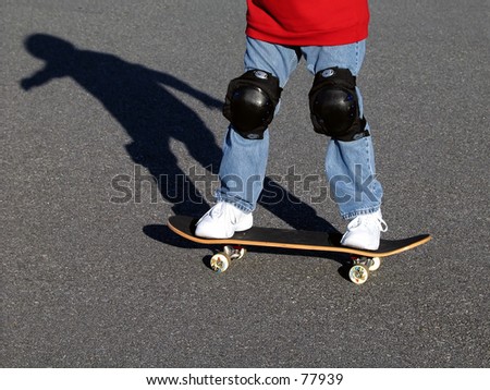 Photograph of a boy on his skateboard showing knee pads, the board, and his shadow