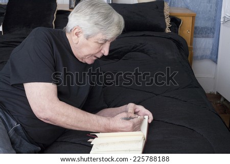 A senior man writes while resting on his bed.