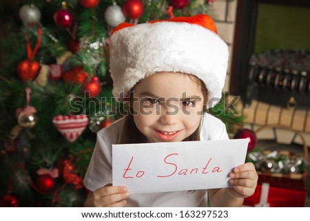 Smiling little girl in christmas hat holding letter for Santa