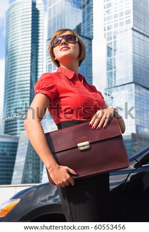 Beautiful businesswoman holding a briefcase near the car on a background of skyscrapers