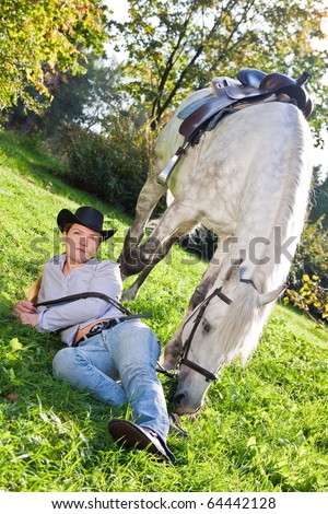 Girl in a cowboy hat lies on the grass near a white horse
