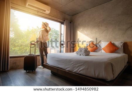 Portrait of tourist woman standing nearly window, looking to beautiful view with her luggage in hotel bedroom after check-in. Conceptual of travel and vacation. ストックフォト © 