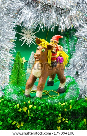 Santa Claus rides a horse in the year of the horse with pink toy ball on background of shiny Christmas trees, snowflakes, stars of gold, and silver tinsel zelynoy
