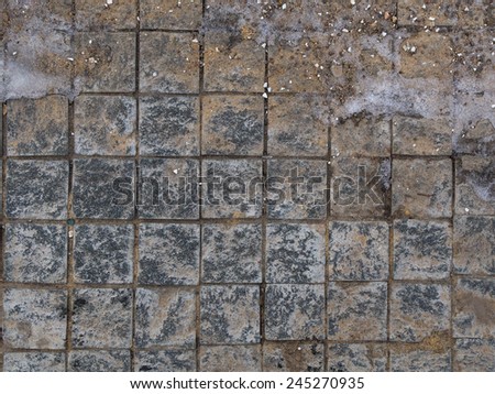 street dirty granite square small gray tiles with rough rough seams and scattered gravel, sand and ice