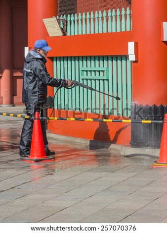 Tokyo - February 4, 2015: Japanese janitor in uniform wash water from a hose building in the capital of February 4, 2015, Tokyo, Japan
