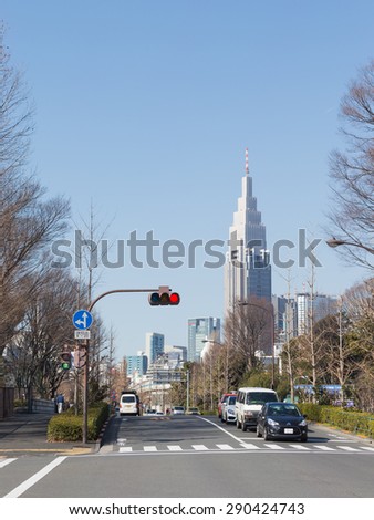 Tokyo - February 6, 2015: cars are at a crossroads at the traffic light is a red light and you can see a tall building and blue sky February 6, 2015, Tokyo, Japan