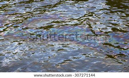 spot of gasoline colored film on the surface of the water in the river polluting the environment and disrupts