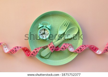 Creative flat lay composition with plate, alarm clock, spoon, fork and measuring tape on pink background. Intermittent fasting, ketogenic, diet concept.  Flat lay, copy space.

