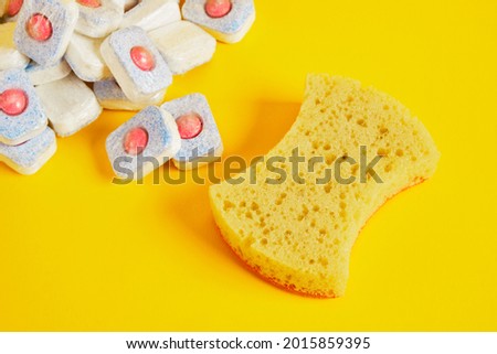dishwasher tablets and dishwashing sponge on yellow background, dishwashing products, hand wash dishes or use dishwasher