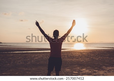 young man at sunset raises his hands up