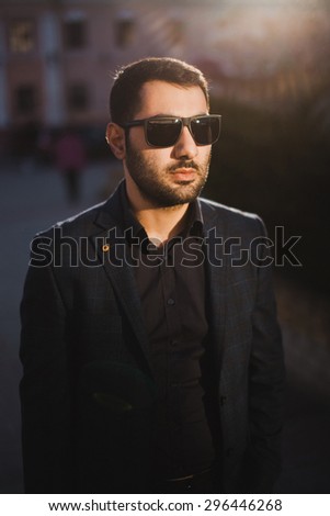a young guy in sunglasses with a beard and a mustache in a suit jacket and posing in hours on the street