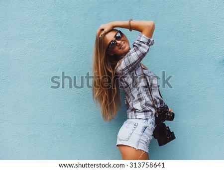 young girl in shorts, no shirt and sunglasses with retro camera takes pictures