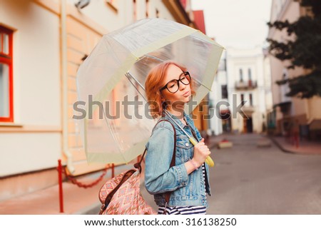 Outdoor street style fashion look at elegant glamour sexy girl,wearing classy mini blue jacket, vintage hipster glasses,posing on the European street, pastel soft colors.Rainy autumn day,playful mood
