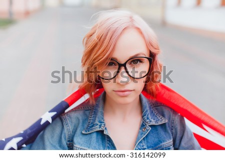 Young beautiful woman posing at the city, holding american flag, wearing crop top and gothic bright make up. Rainy day,amazing colored hairs.California,LA