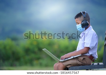 Asian elementary school-aged boys living in rural areas and schools in rural Thailand. Wear a mask to prevent the coronavirus (COVID 19) elementary school children online using a laptop to watch.
