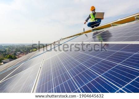 An engineer uses a laptop computer to inspect solar panels on the roof of a house where solar panels are installed using solar energy.