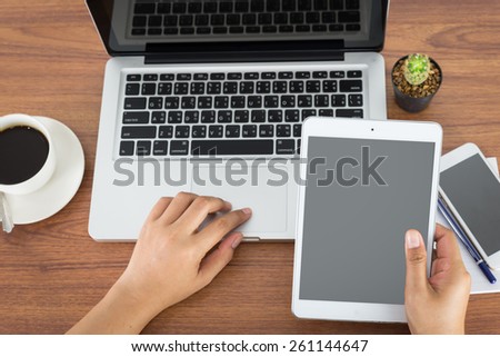 female hands holding a computer tablet and laptop on the table in the office