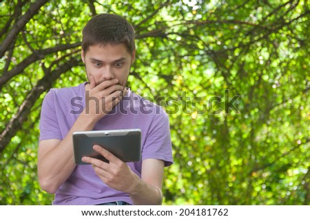 Surprised young man looking at a tablet computer in a summer park