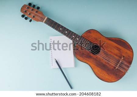 Little guitar and blank notebook with pencil on the azure surface