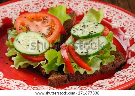 Rye sandwich with salad leaves, tomato, cucumber, bell pepper in red plate closeup