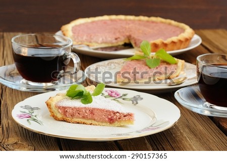 Strawberry tart with two cut pieces decorated with fresh mint and two glass cups of black tea