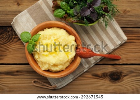 Polenta with basil shoot in wooden bowl with green salad and wooden spoon on striped rustic cloth and old wooden table
