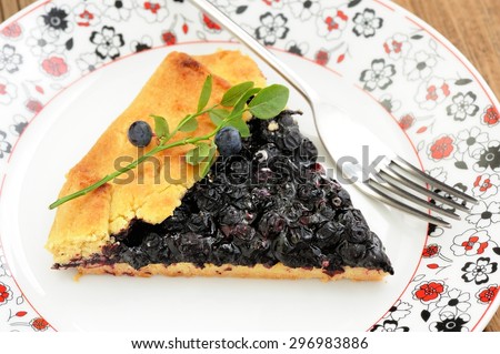 Piece of homemade vegan galette with wild blueberry on painted plate with fork decorated with green blueberry twig