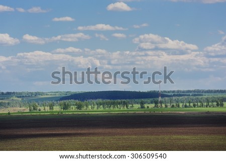 Wide field with distant trees and blue sky with white clouds