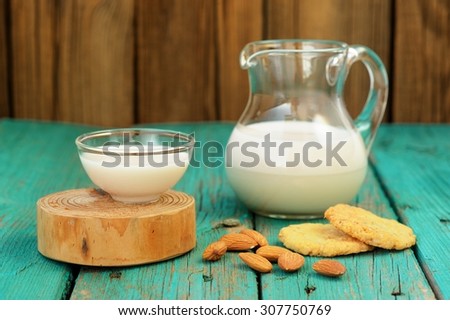 Homemade fresh almond milk in glass jar and glass bowl, with homemade almond cookies and whole almonds on shabby turquoise wooden table