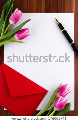 Blank card, red envelope, pen and tulips on a wooden background