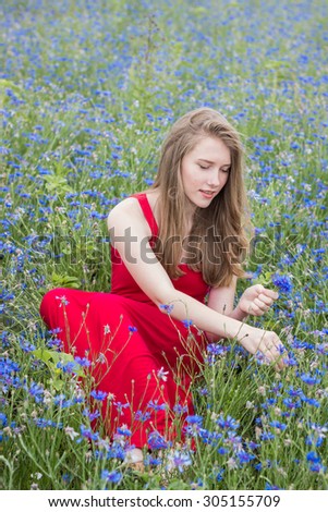 Young beautiful smiling girl picking flowers in the meadow, outdoor portrait