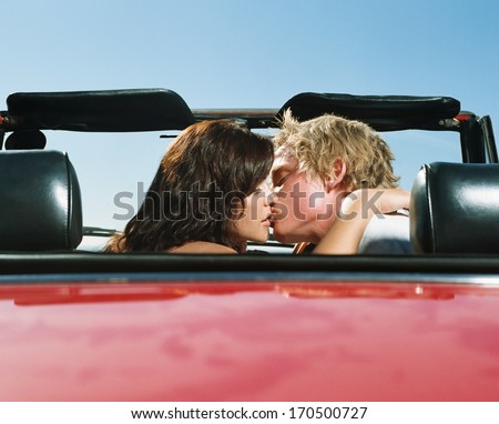 Young couple kissing in a red car
