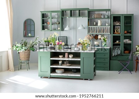Green kitchen interior with furniture. Stylish cuisine with flowers in vase. Wooden kitchen in spring decor. Cozy home decor. Kitchen utensils, dishes and plate on table. kitchen island in dining room