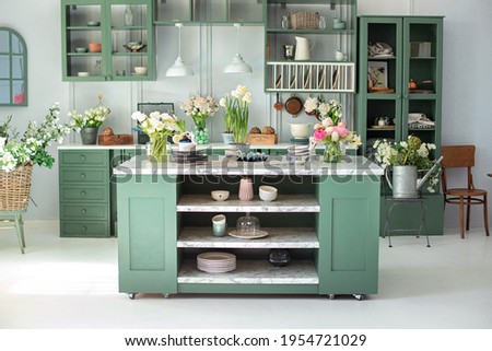 Green kitchen interior with furniture. Stylish cuisine with flowers in vase. Wooden kitchen in spring decor. Cozy home decor. Kitchen utensils, dishes and plate on table. kitchen island in dining room